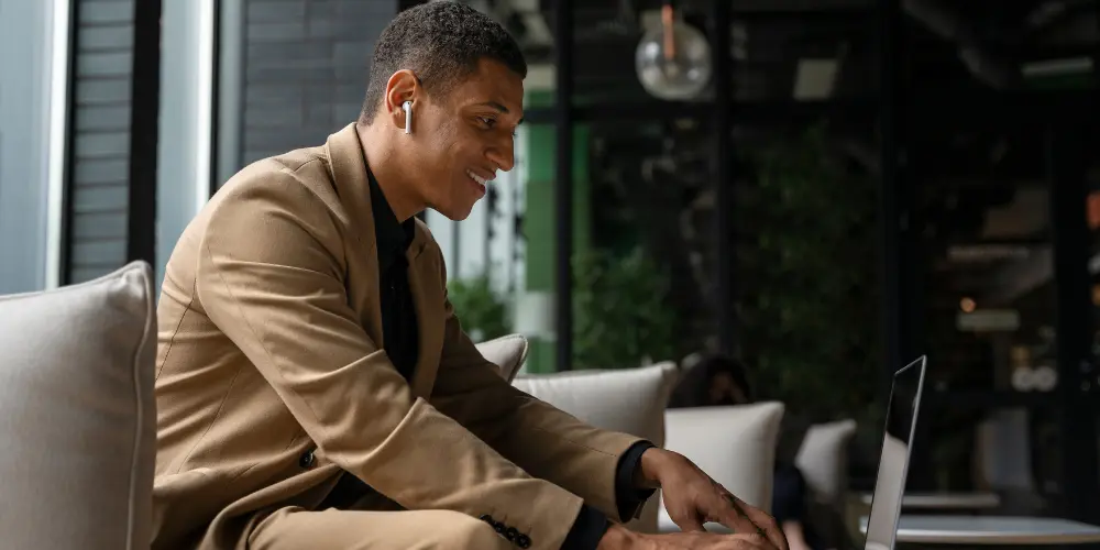 Professional man with earbuds smiling while working on laptop — Real-World Learning Builds Career Confidence