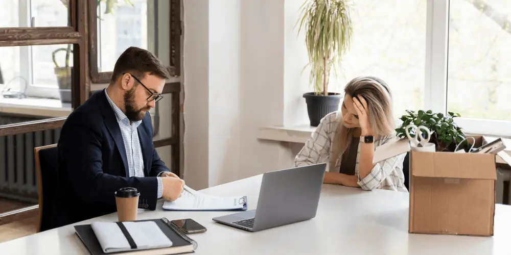 Stressed employee at a desk with a cardboard box after a layoff — how to handle a layoff and face the job search