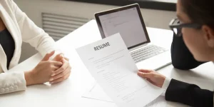 Professional handing over a resume document at a desk during a job interview — how to ensure job security with a standout resume