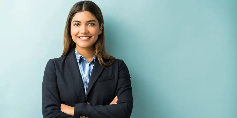 Confident professional woman in blazer with arms crossed against teal background — how to build a personal brand