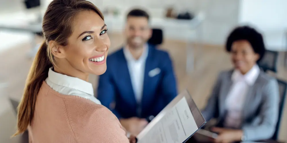 Smiling woman holding documents in a job interview setting - how to get ready for the hiring season with resume and job search tips