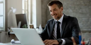 Professional man smiling at a laptop in an office - simple ways to stay active on LinkedIn anytime