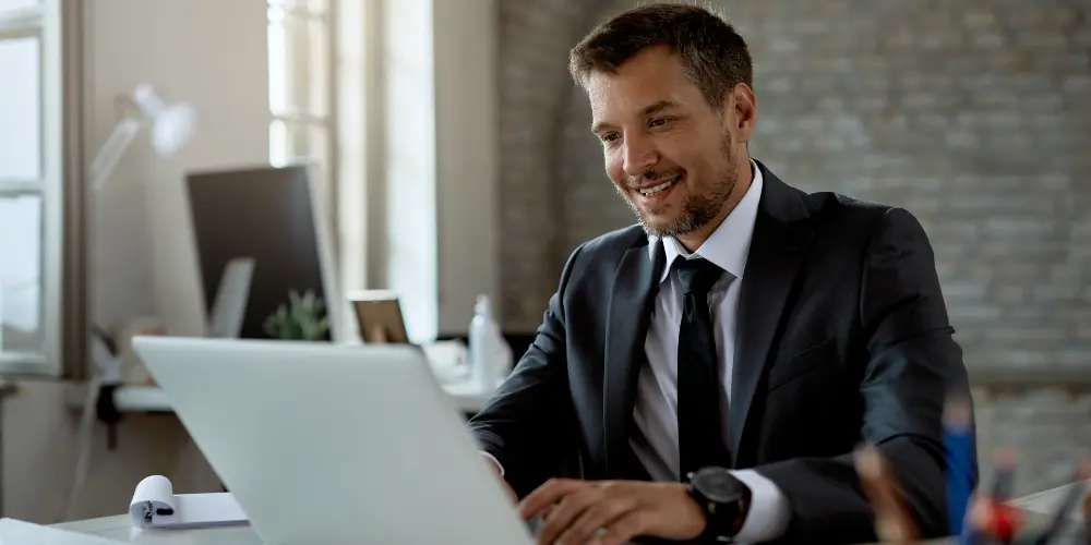 Professional man smiling at a laptop in an office - simple ways to stay active on LinkedIn anytime
